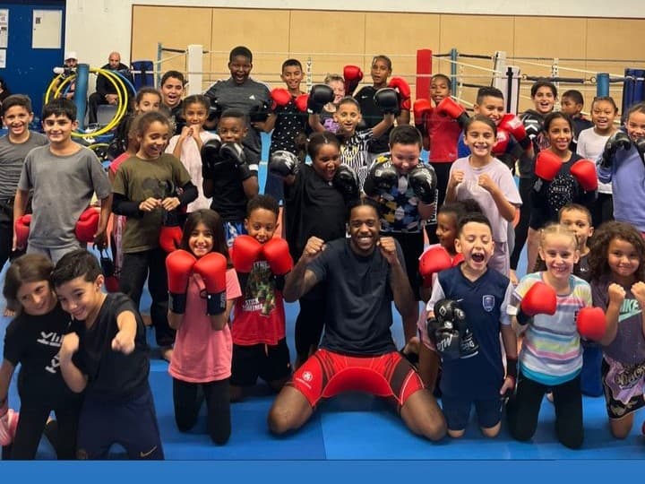 Groupe d'enfants en gants de boxe rouges autour de leur coach, sur les tatamis du gymnase.
