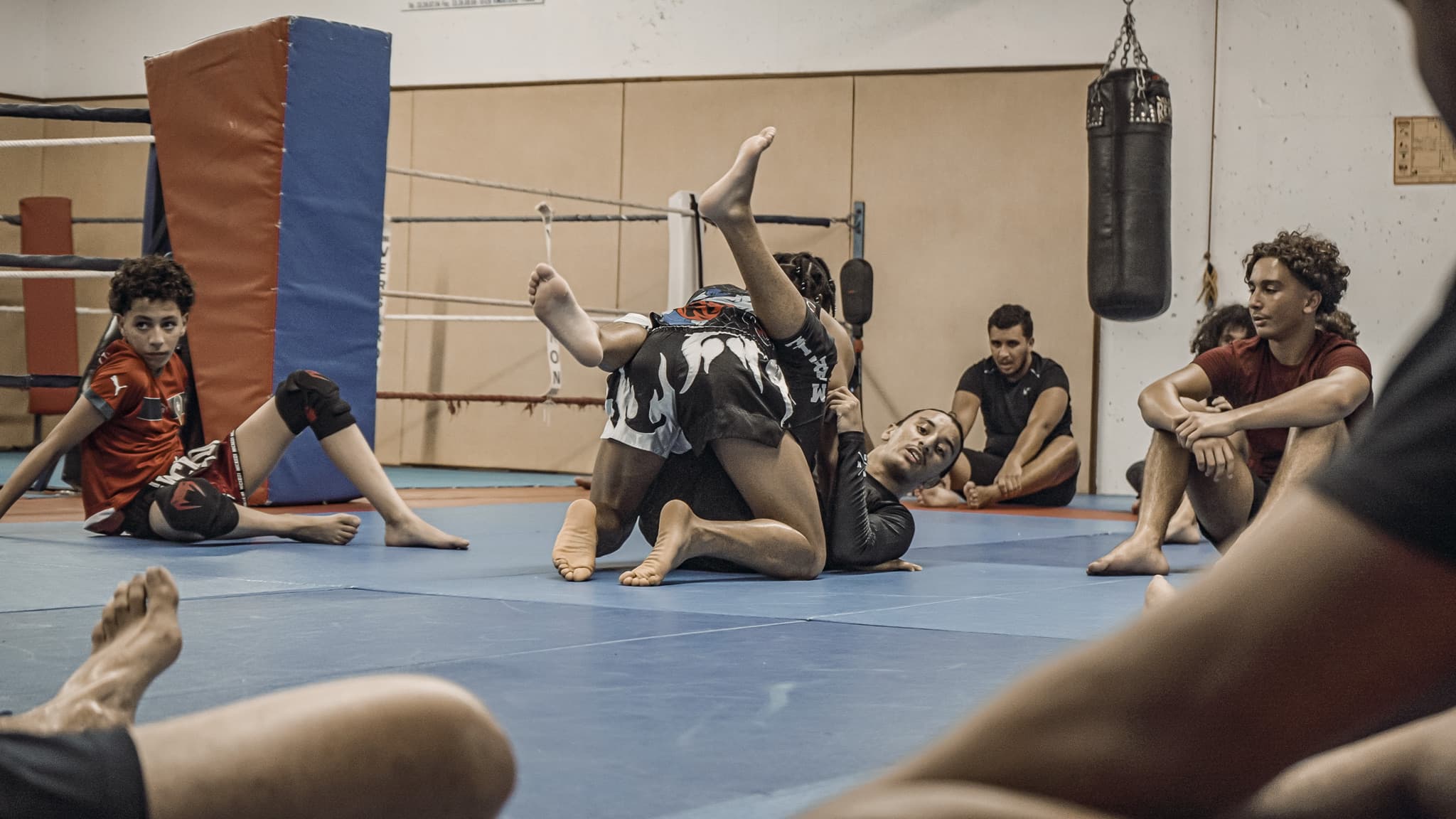 Séance de grappling à l'Aquila Academy : deux pratiquants au sol devant le groupe, dans la salle du gymnase.